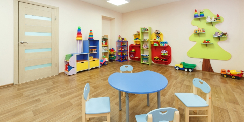 A kindergarten classroom is occupied with colourful chairs, tables, cub board, toys and shelves.