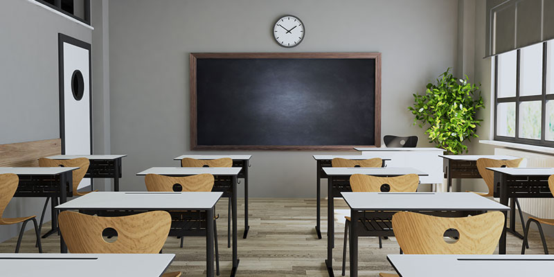 A school classroom equiped with modern wooden tabls and chairs along with teaching mateirals such as blackboard, clock and indoor plants.