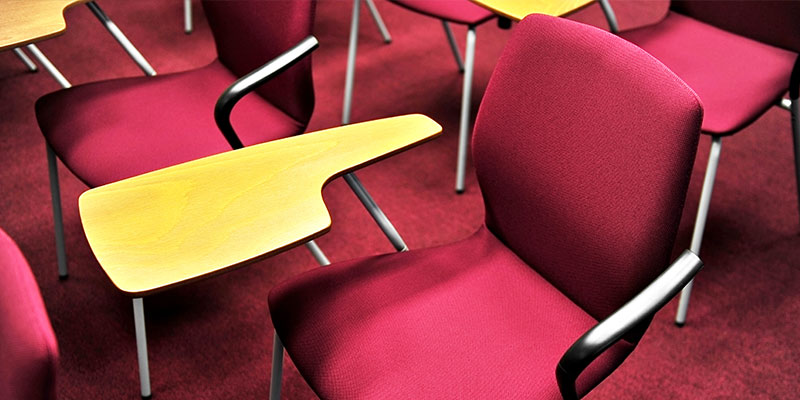 An empty student chair with a wooden writing pad in a conference room.