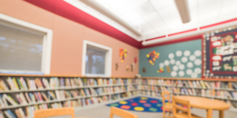 A blurred image of a kid reading corner in a school library interior with children books for leisure reading on bookshelves.