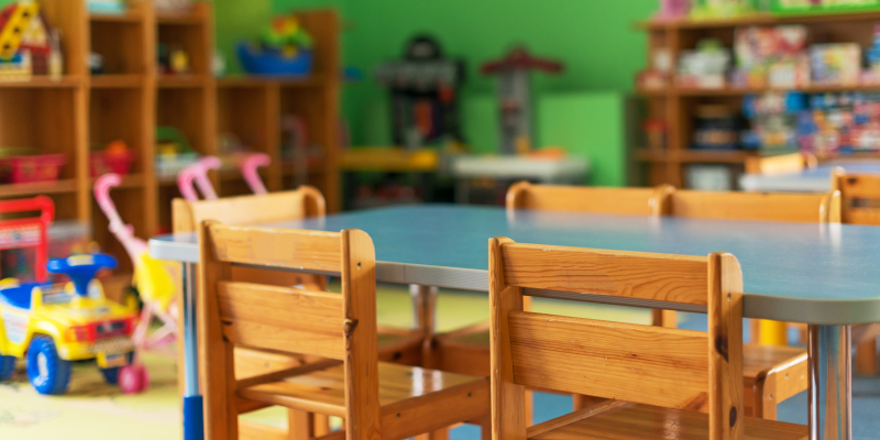 "The interior of a kindergarten classroom with chairs, tables and tops."